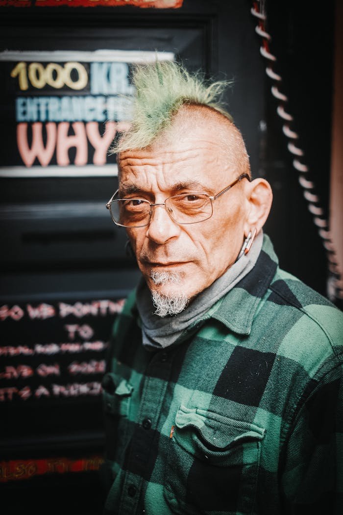 menu-01 Expressive portrait of an elderly man with a green mohawk, wearing eyeglasses and a flannel shirt.