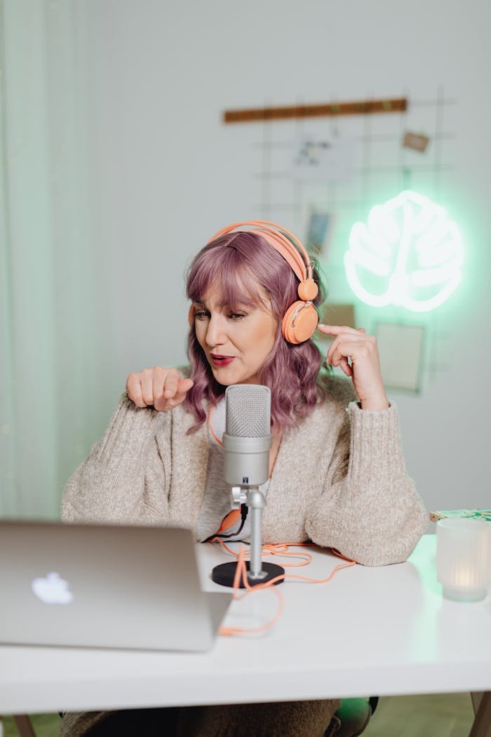 menu-03 A woman recording a podcast indoors with a laptop and microphone, wearing headphones.